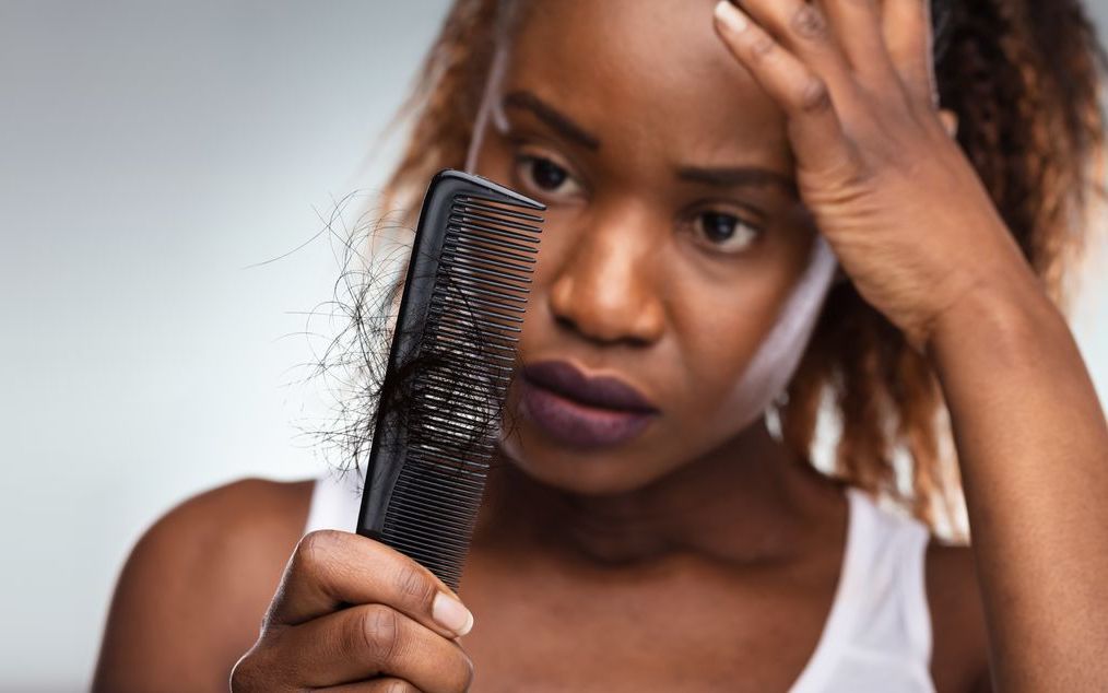 A woman is holding a comb and looking at her hair.