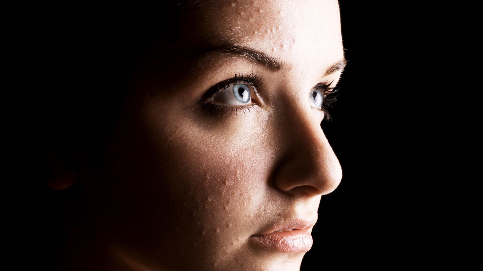 Side-profile portrait of a person in dramatic low light, looking right with a neutral expression.
