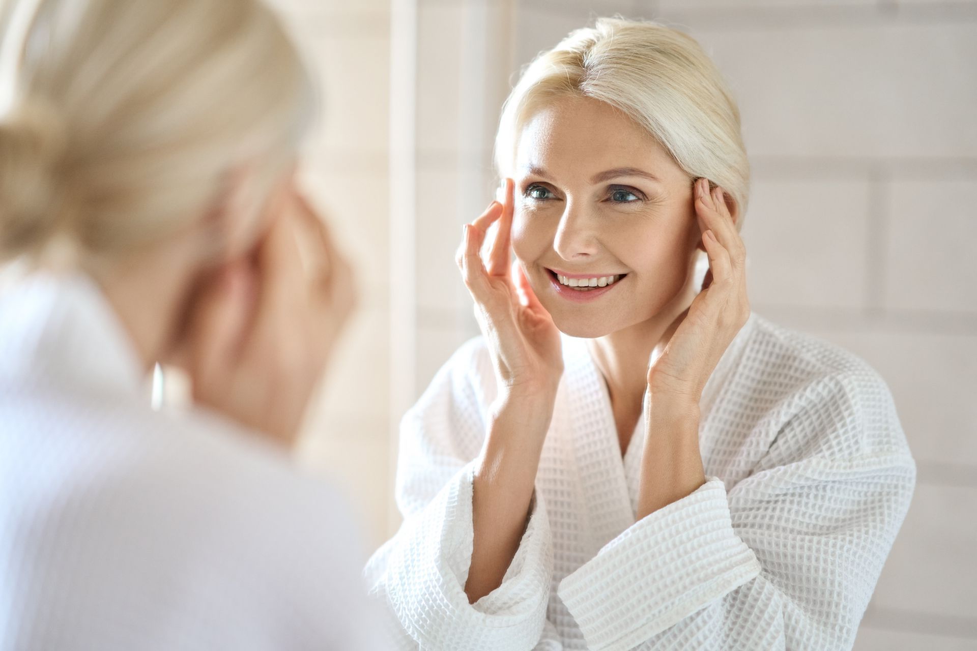 mature woman examines her skin while looking in the mirror after skin tightening treatment