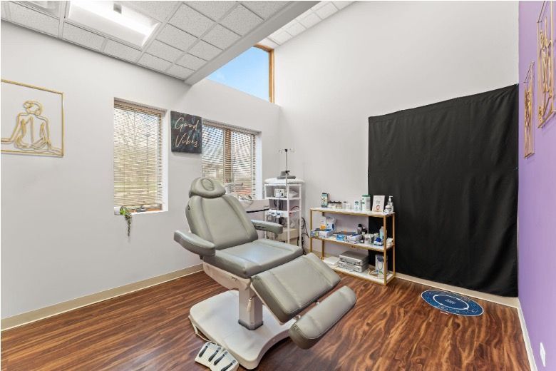 Empty dental treatment room with reclined gray chair, wood floor, and black privacy curtain.