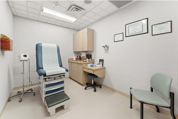 Medical exam room with exam table, desk, chair, and wall charts
