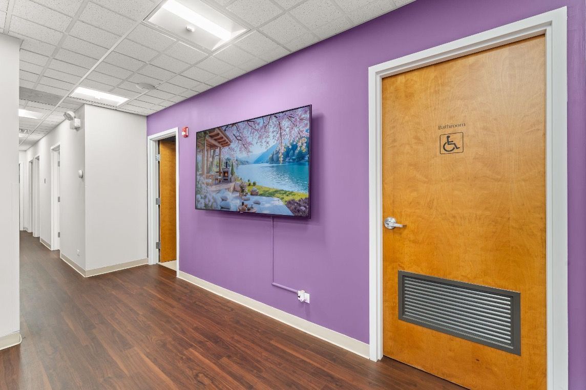 Bright office hallway with purple wall, mounted TV, wood floor, and wooden door with vent panel