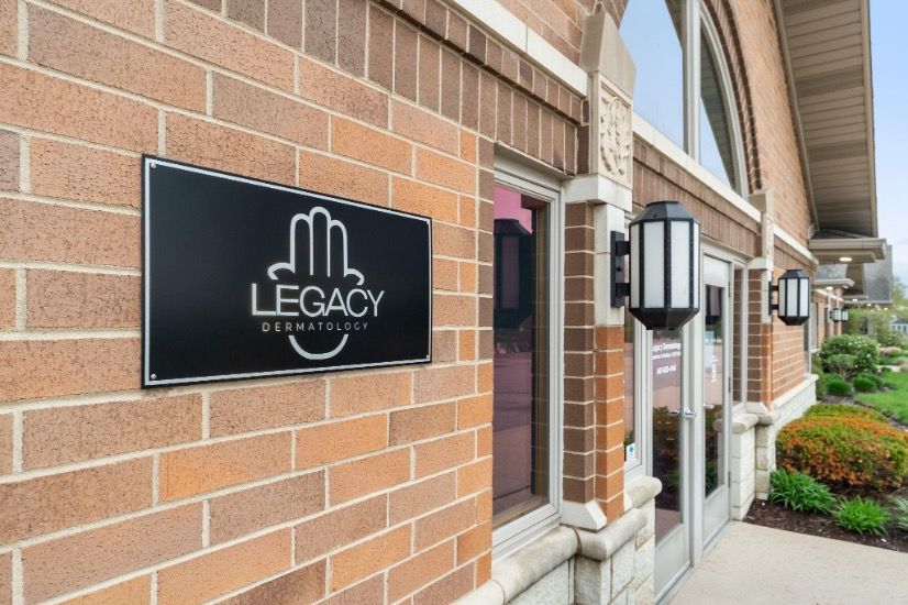 Brick building entrance with a black “LEGACY” sign and nearby wall-mounted lanterns.