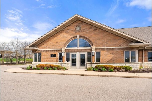 Brick building entrance with large arched window, glass doors, and flower beds under a blue sky