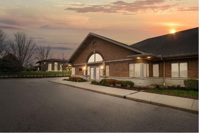 Brick building at sunset with arched entrance, lit windows, and empty parking lot