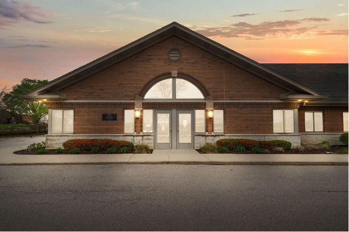 Brick building with arched entrance at sunset, framed by flower beds and parking lot.