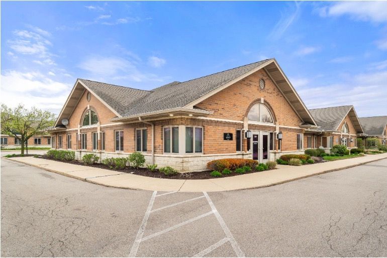 Brick office building with arched windows and a sloped roof beside a paved parking lot