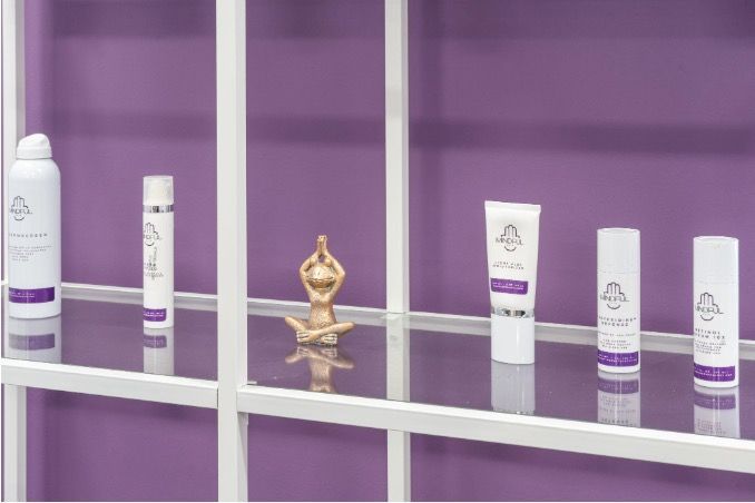 Purple product display with white tubes and bottles on shelves, centered around a small gold ornament
