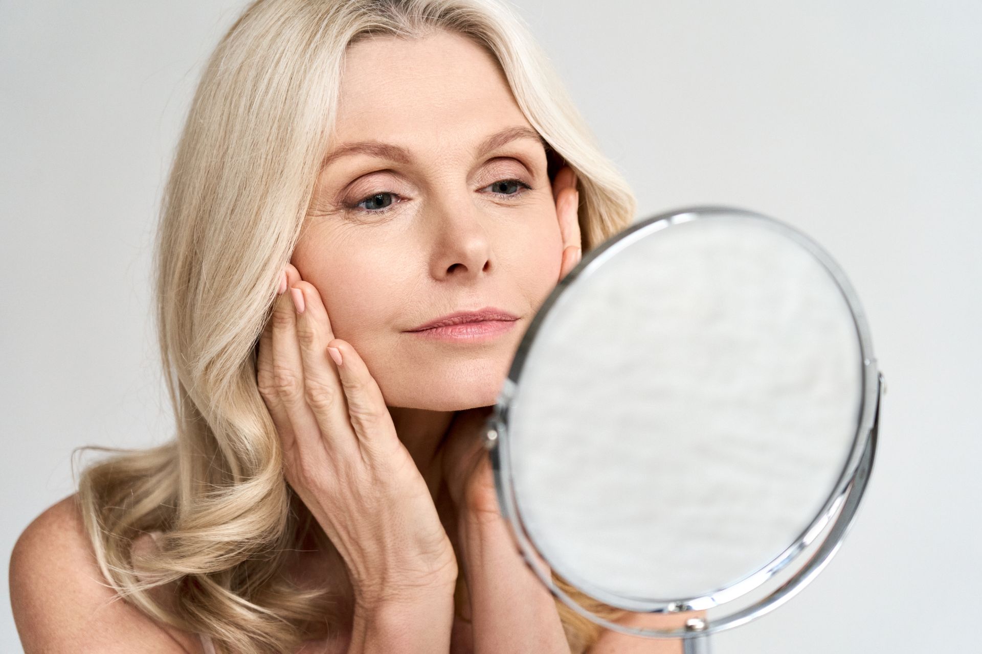 mature white woman looks at facial wrinkles in mirror