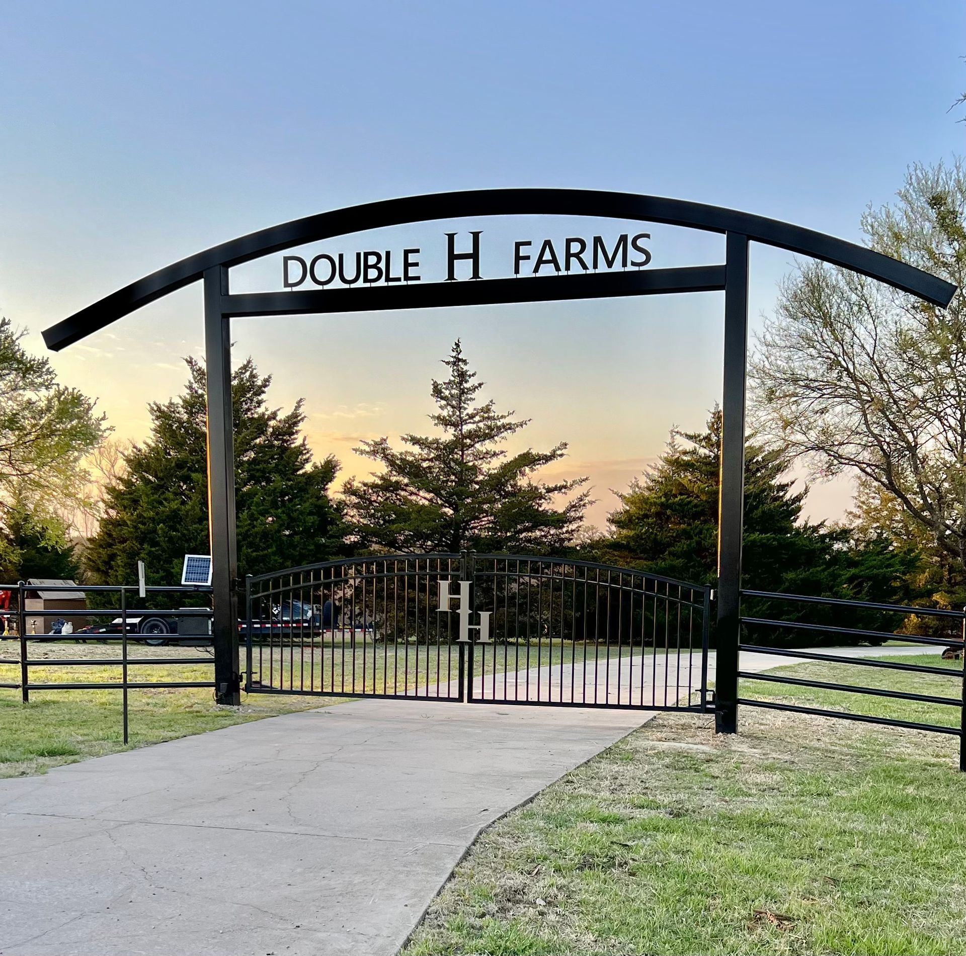 A sign for double h farms is above a gate
