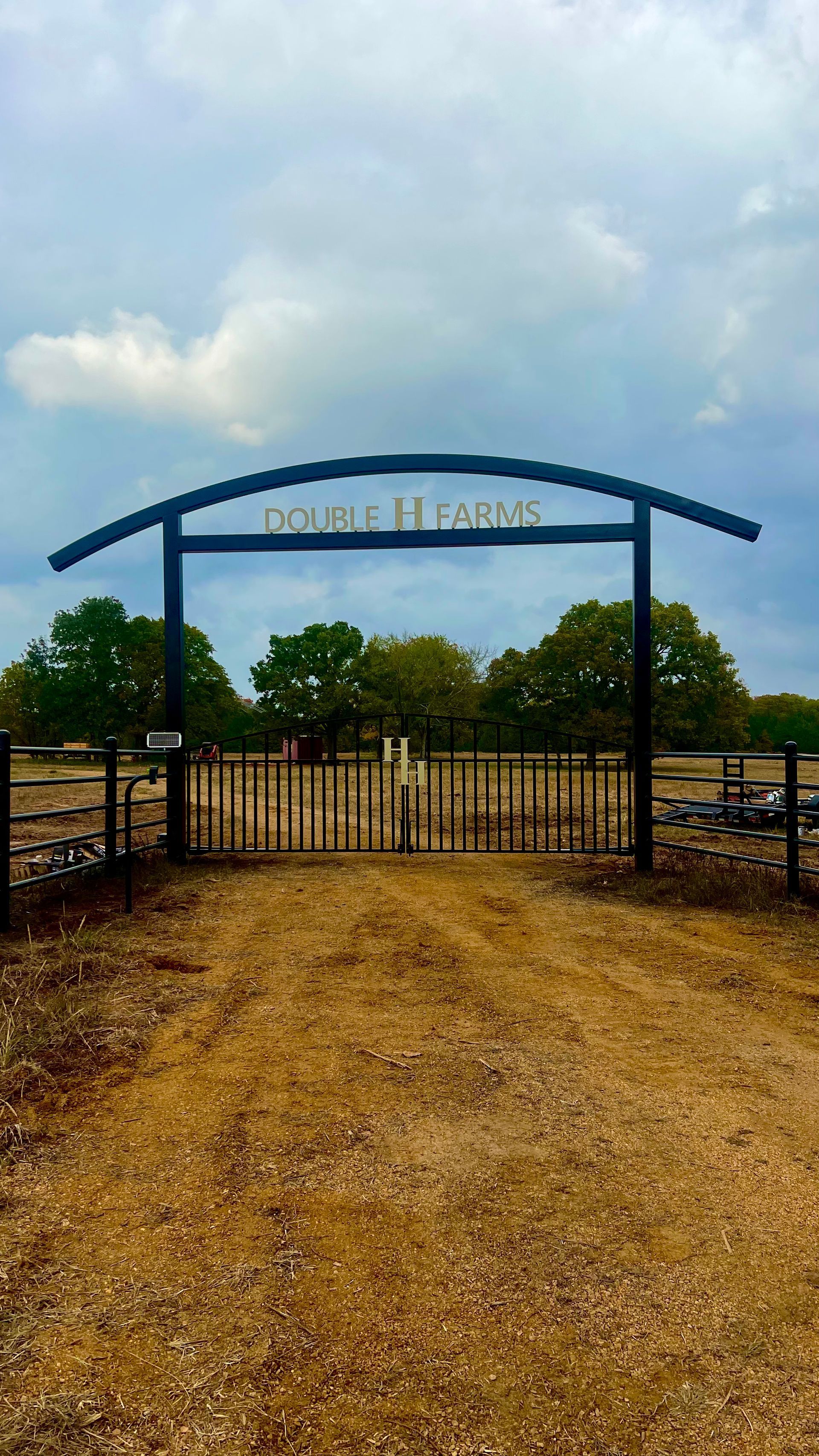 There is a gate in the middle of a dirt road.