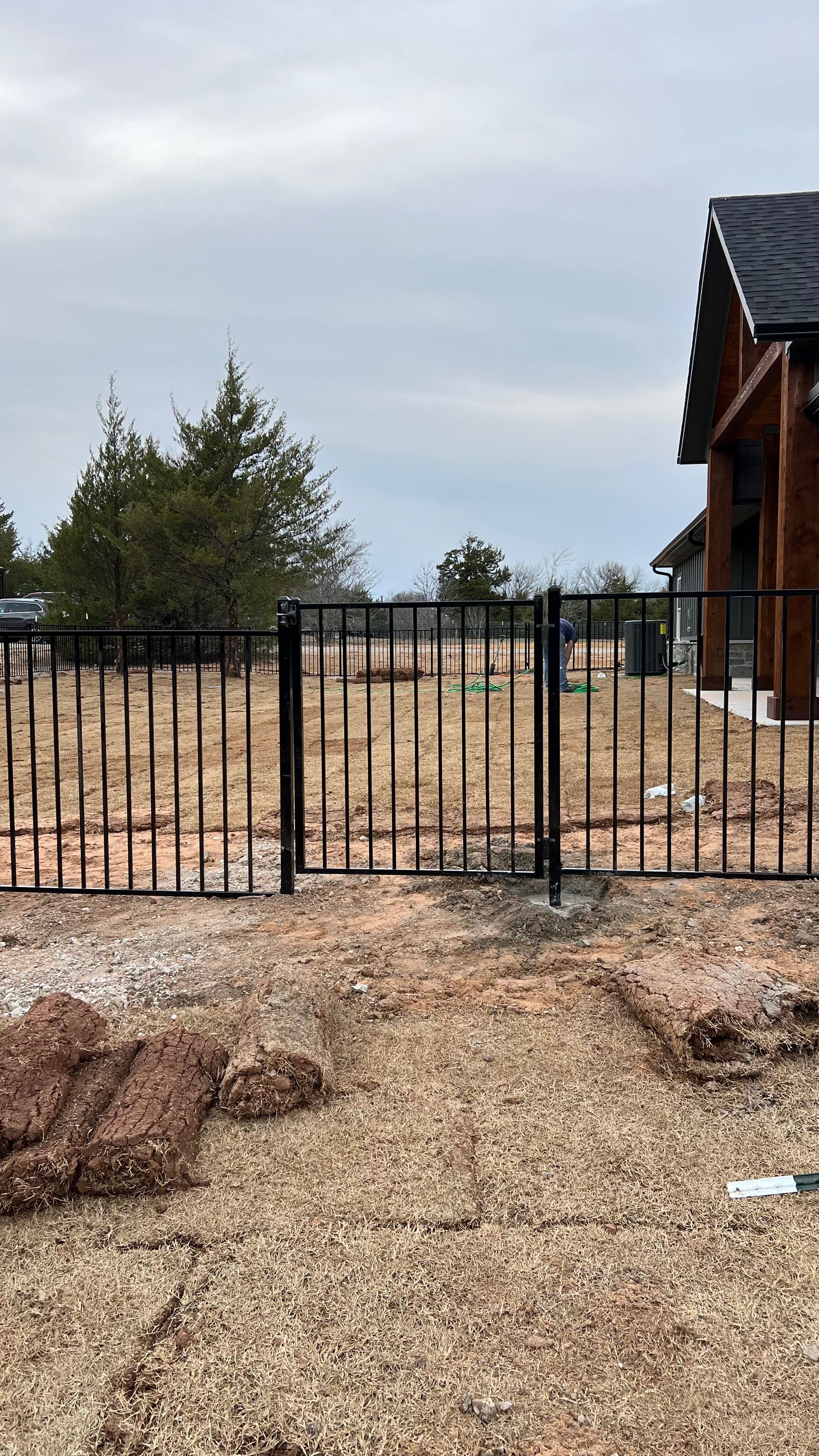 A metal fence is surrounding a dirt field in front of a house.