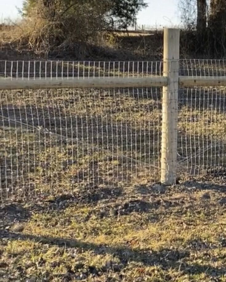 A wooden post and wire fence in a field.
