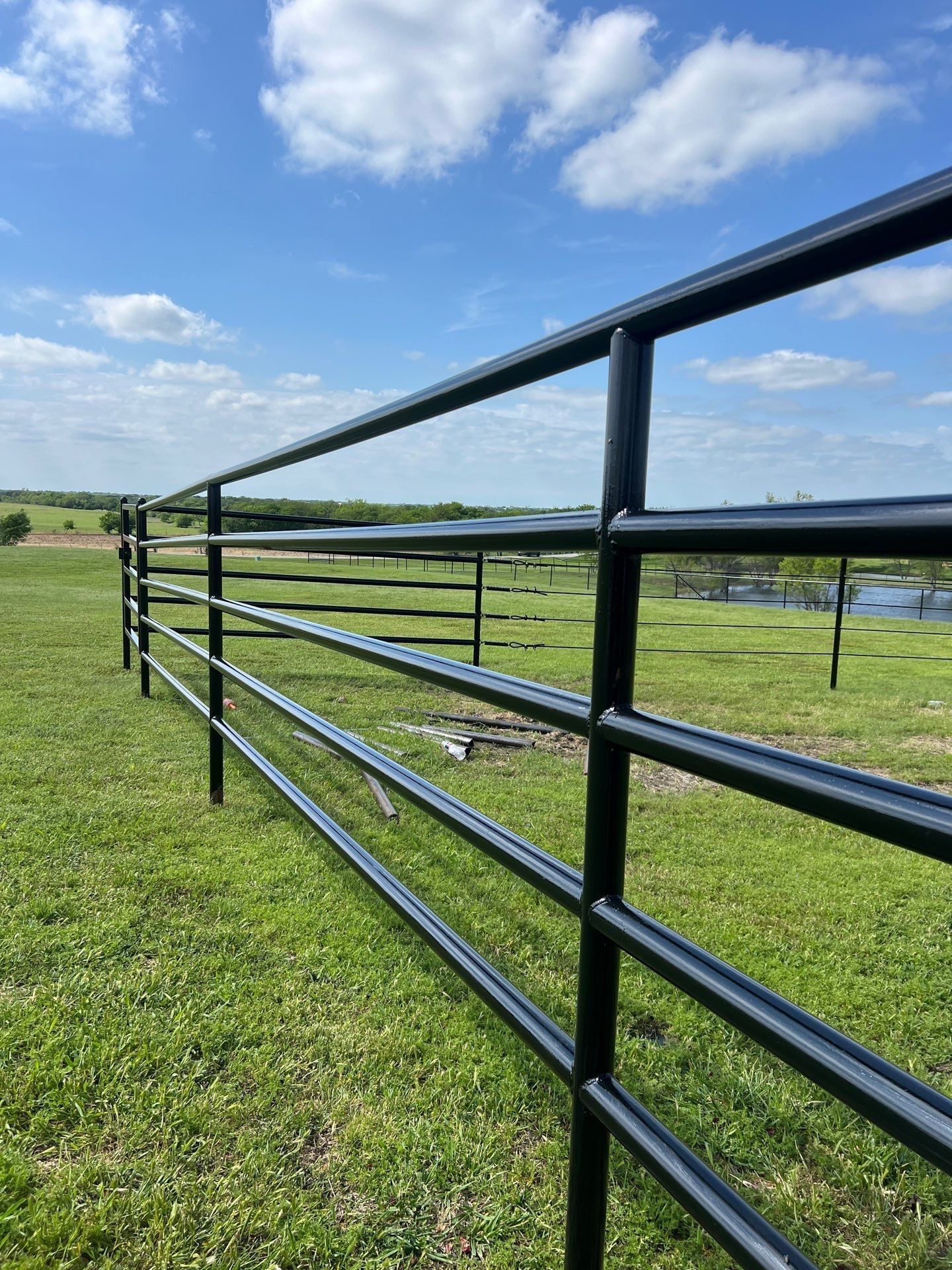 A black metal fence is in the middle of a grassy field.