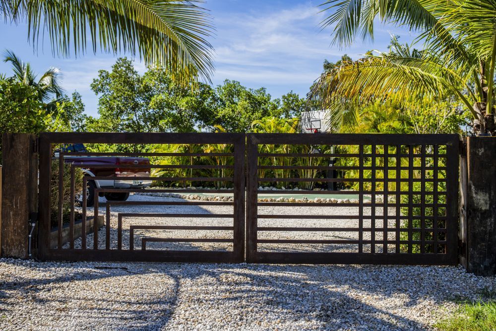 A metal gate is surrounded by palm trees and gravel.
