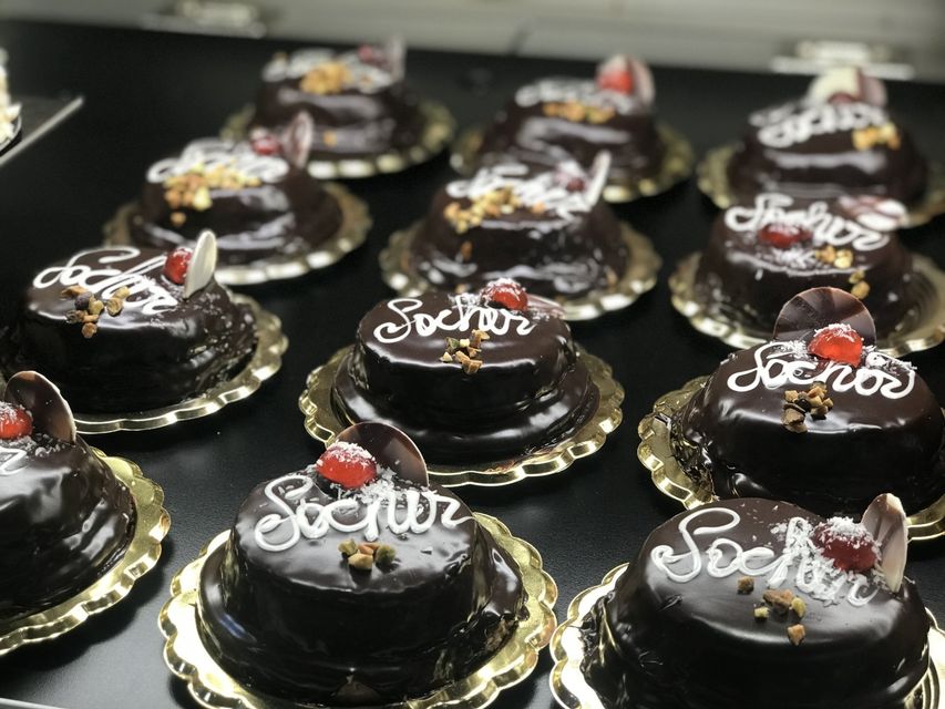 In mostra torte al cioccolato con glassa bianca su cui è scritto "Sochos", guarnite con ciliegie e noci.