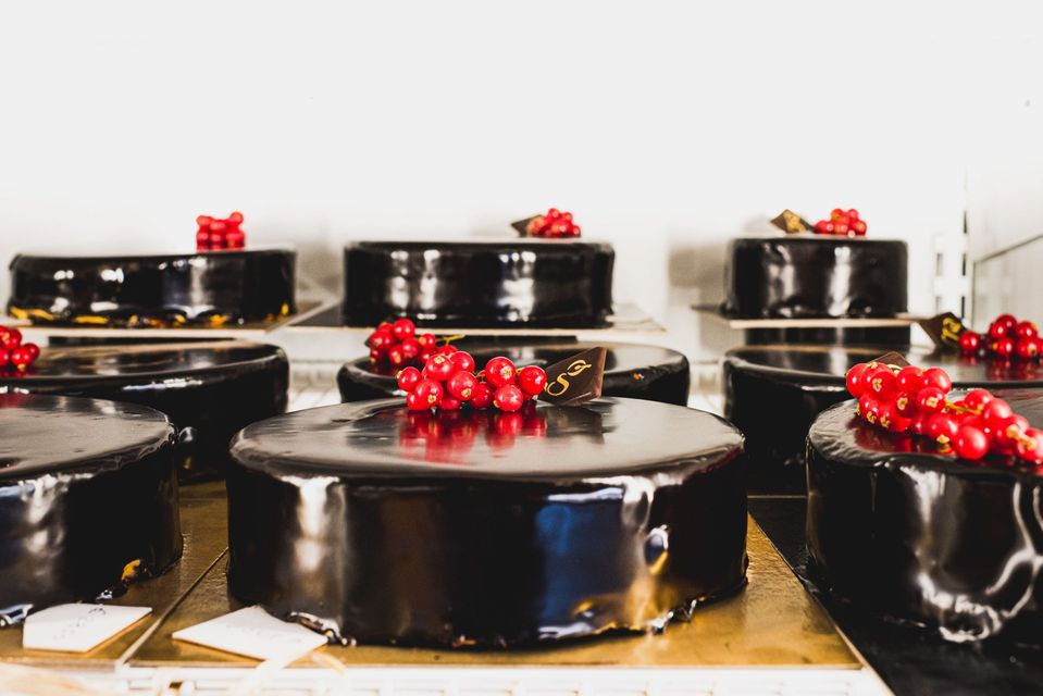 Torte con glassa lucida al cioccolato fondente, guarnite con frutti di bosco rossi, esposte in un ambiente da pasticceria.