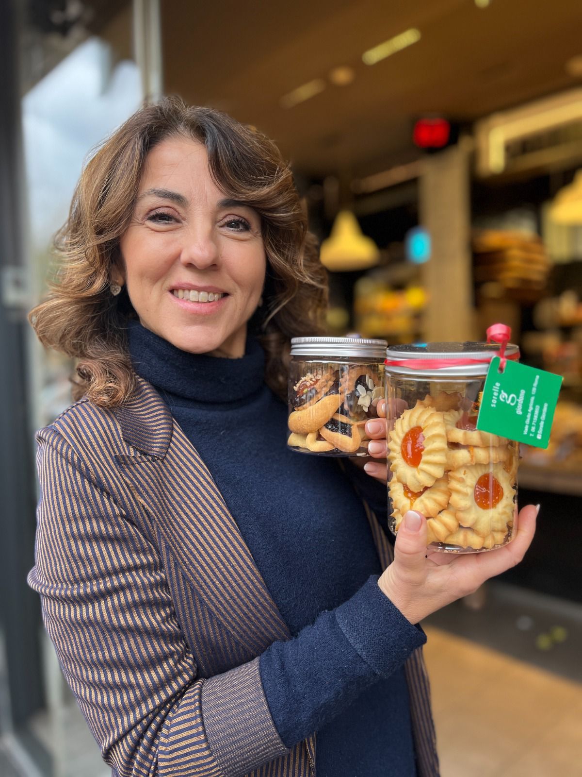 Donna sorridente, con in mano due barattoli di biscotti, in piedi fuori da un negozio.