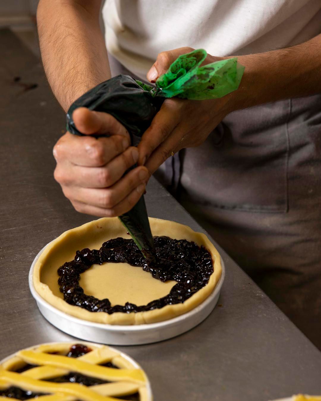 Persona che versa il ripieno nella crosta di una torta. Ripieno scuro in una tortiera bianca.