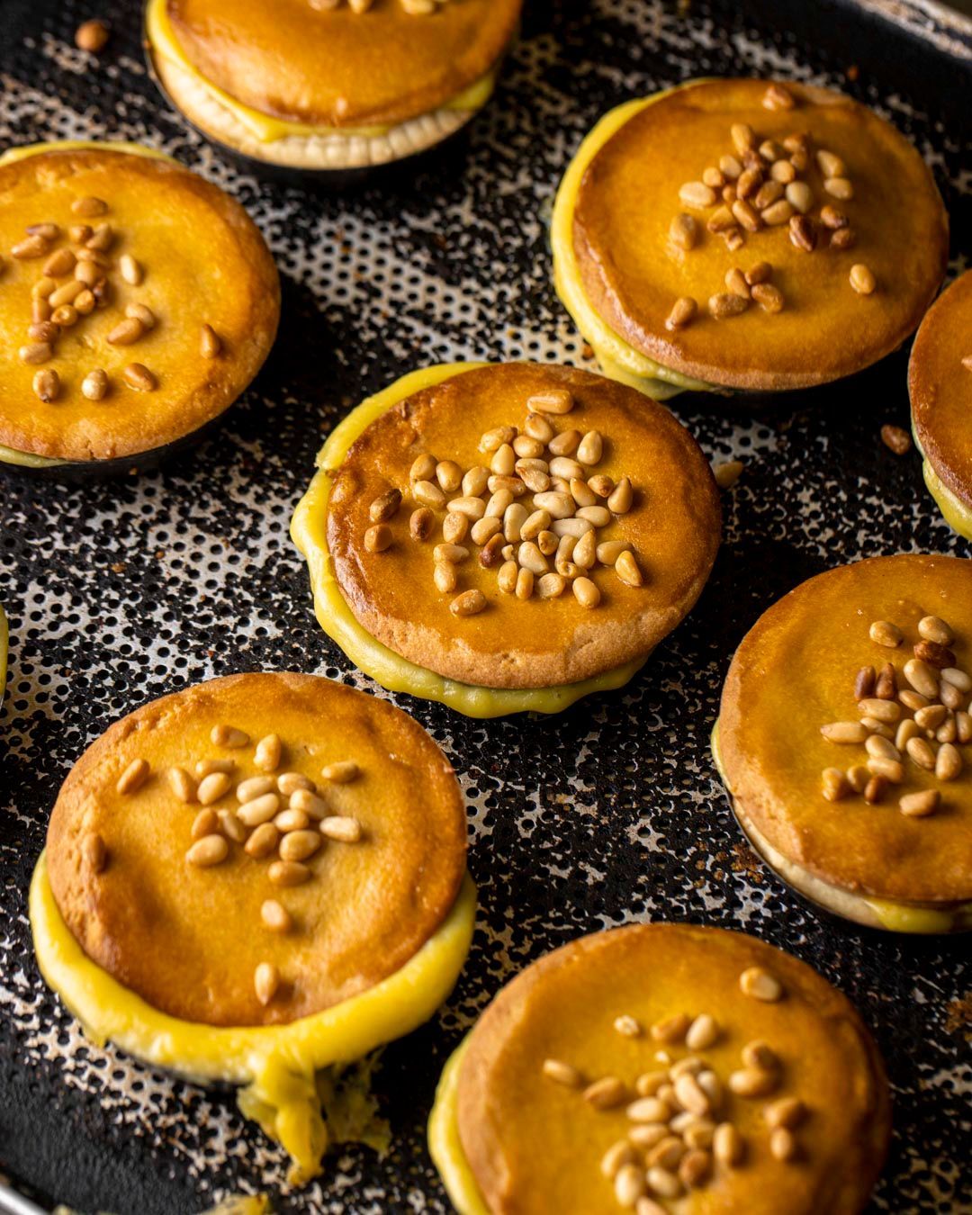 Biscotti su una teglia, dorati, con ripieno e guarniti con pinoli.