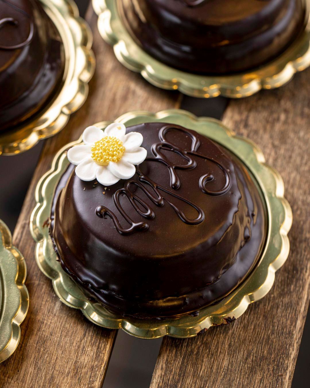 Mini tortine al cioccolato con glassa e fiore decorativo su piatto dorato smerlato.