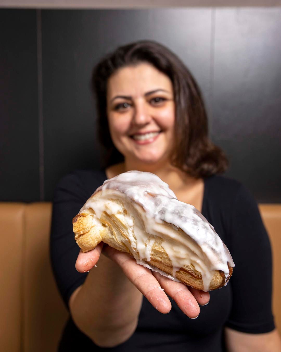 Donna sorridente che tiene in mano un dolce glassato. Top nero, sfondo neutro.