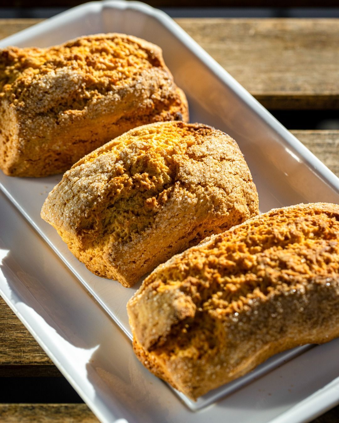 Tre scones rettangolari dorati su un piatto rettangolare bianco, su una superficie di legno.
