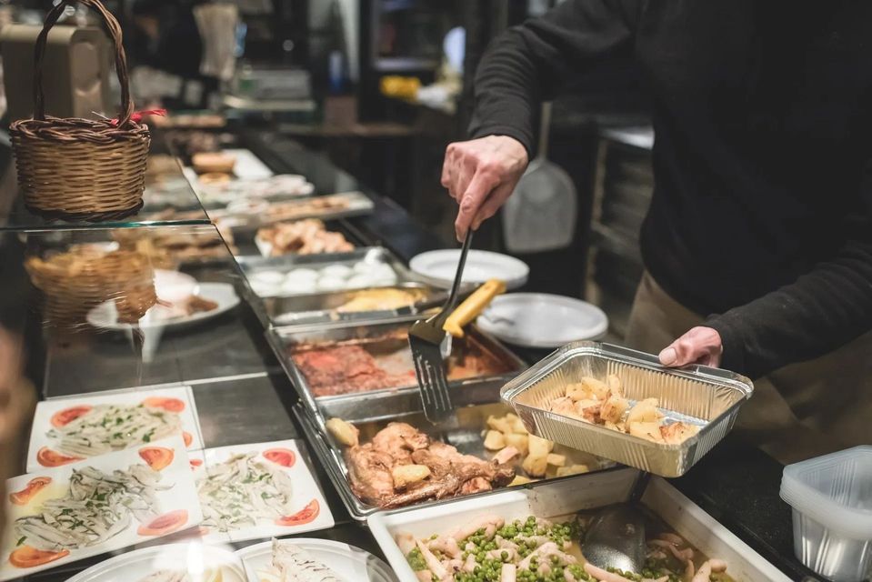 Una persona serve cibo da un buffet. Sono visibili patate, pollo e altri piatti.
