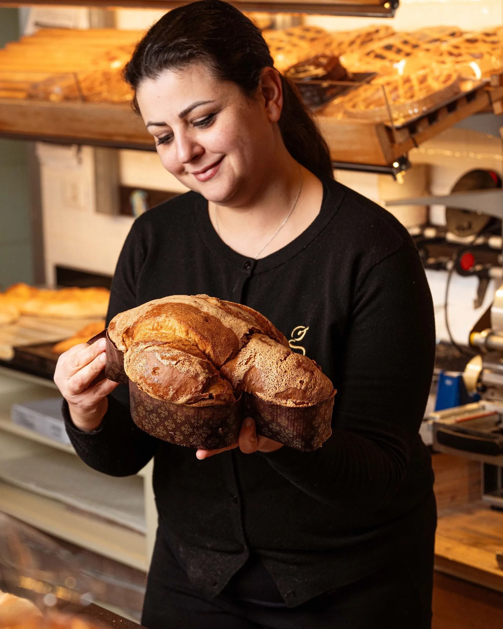 Donna in una panetteria che tiene in mano una grande pagnotta rotonda, sorridente.