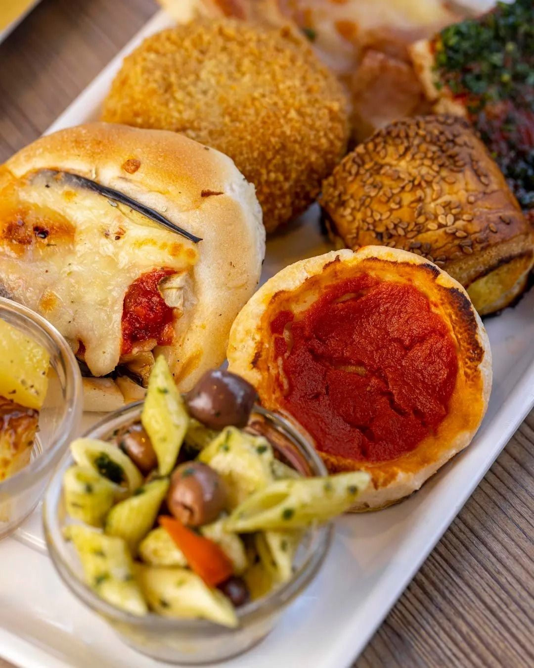 Piatto di antipasti con insalata di pasta, mini pizze e panini ripieni.
