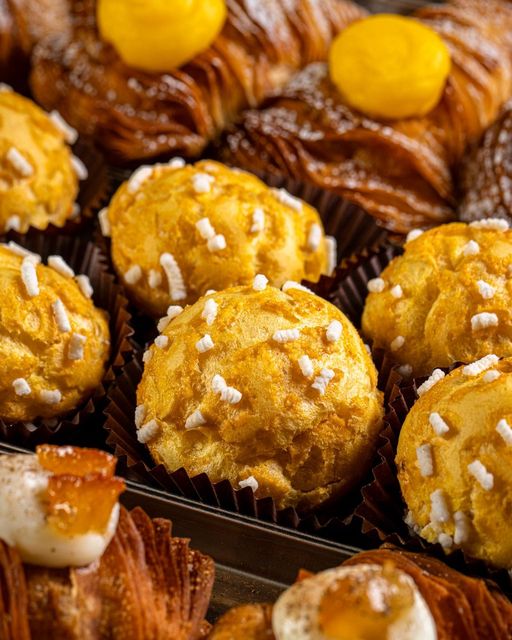 Primo piano di pasticcini assortiti esposti in una vetrina: bignè con granella di zucchero e croissant ripieni.