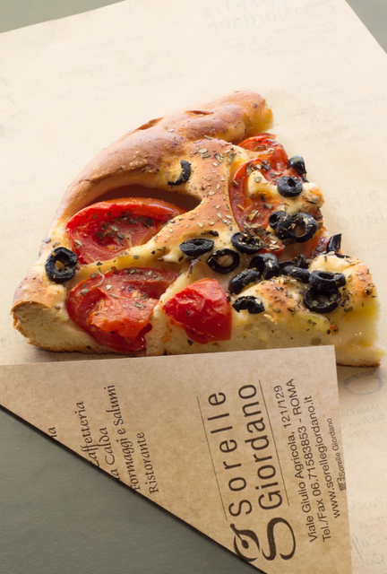 Trancio di pizza con pomodori e olive su carta con stampato il logo del ristorante "Sorelle Giordano".