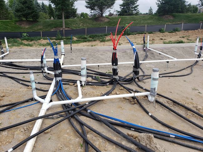 Wiring and pipes on gravel ground, with blue, white, and black cables, possibly for utilities.