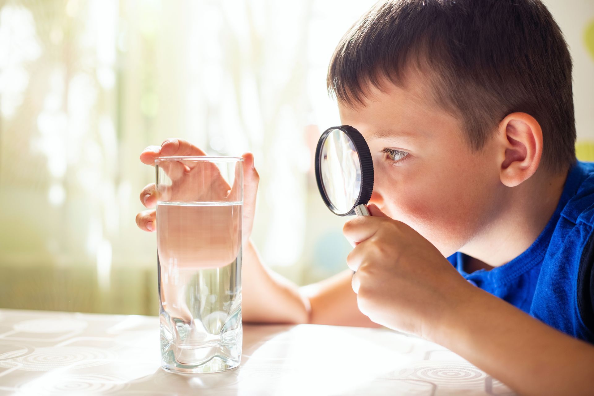 Child examining a glass of tap water with a magnifying glass, illustrating water quality in Tomball, TX Child examining a glass of tap water with a magnifying glass, illustrating water quality in Tomball, TX