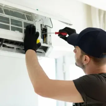 Technician using a screwdriver to repair a wall-mounted air conditioner filter and panel