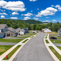 Suburban street with new houses, sidewalks, green lawns, and a blue sky with clouds