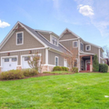 Suburban beige two-story house with white trim, garage, and green lawn under a blue sky