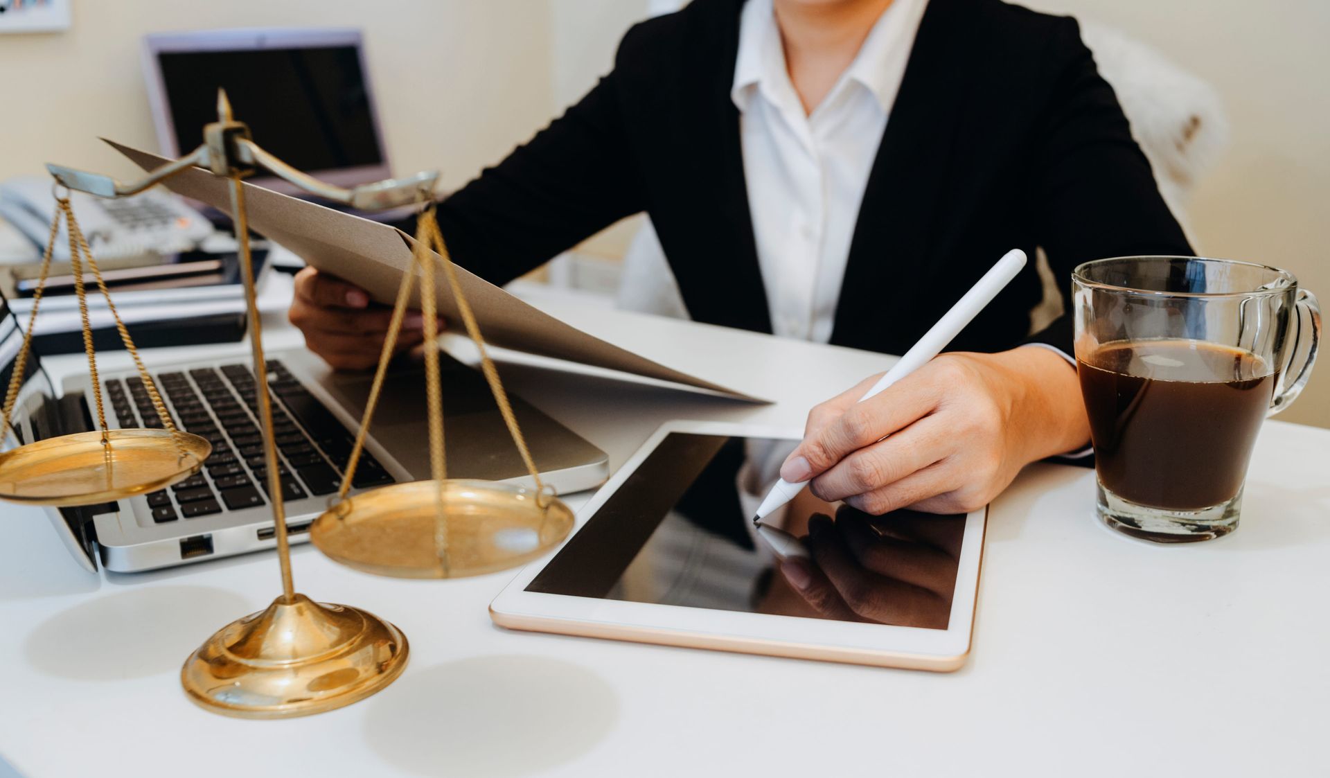 Businessperson reviewing documents with tablet, scales of justice, and coffee on a desk