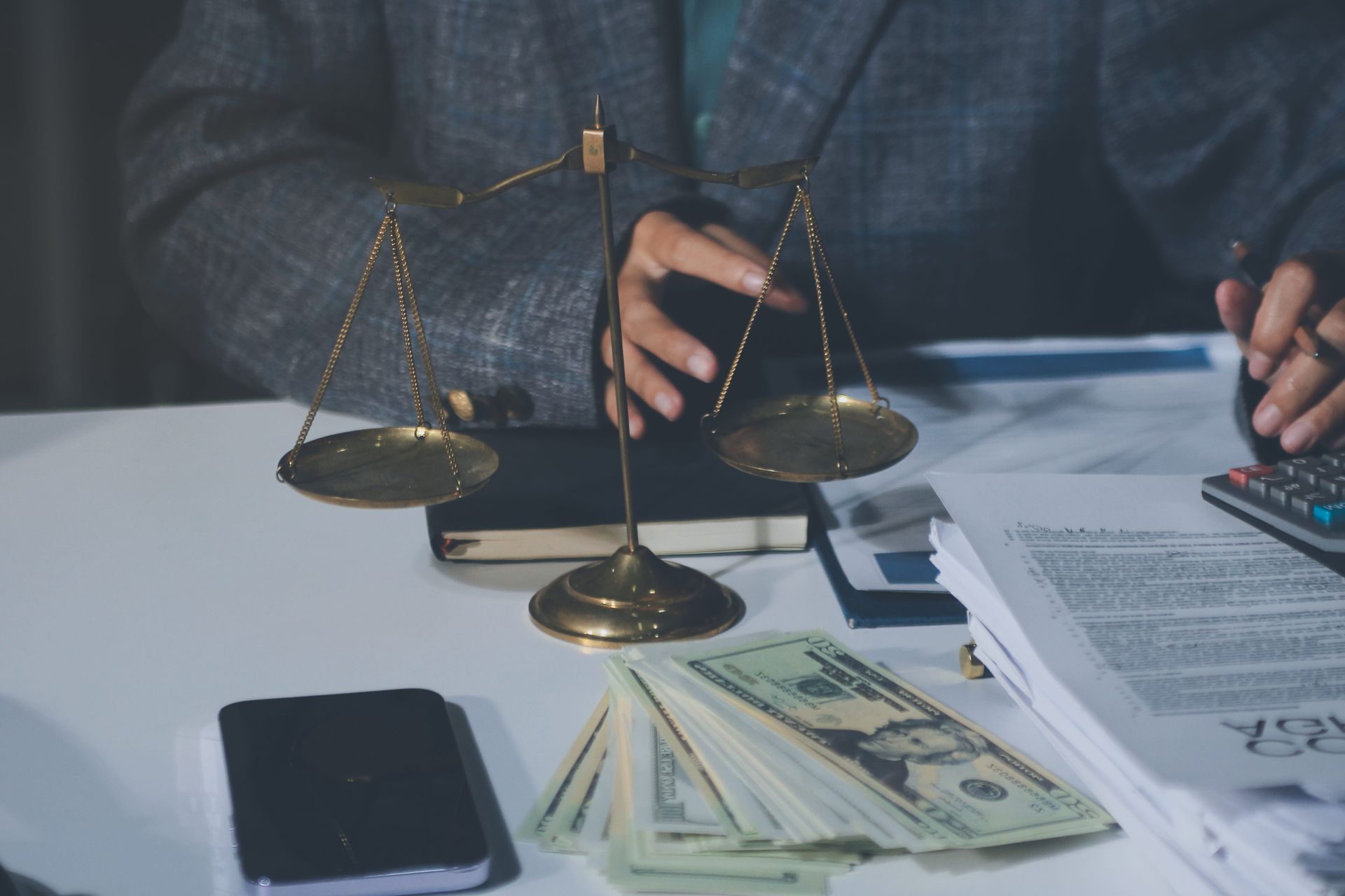 Hands weighing money on a desk beside legal papers, a phone, and a calculator