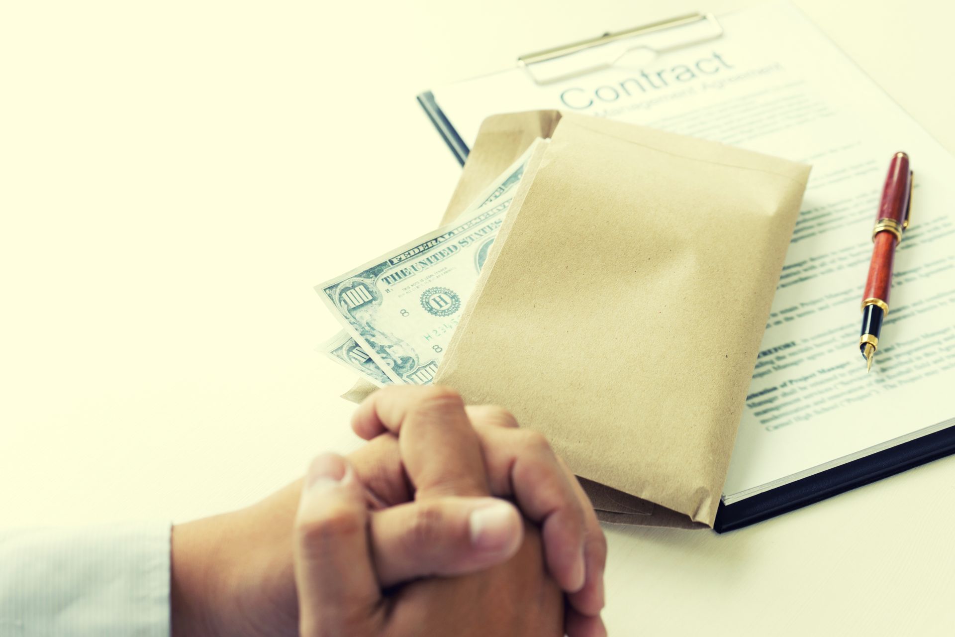 Hands clasped near a contract, a brown envelope, and cash, implying a bribe.