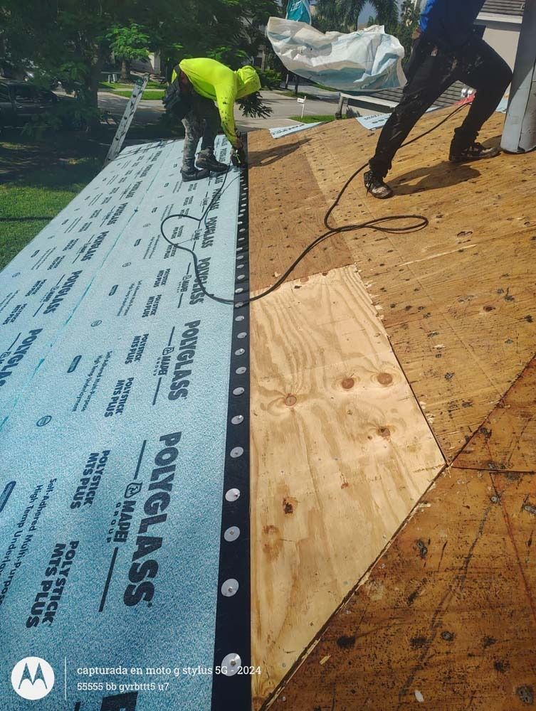 Two workers install blue Polyglass underlayment on a plywood roof deck.