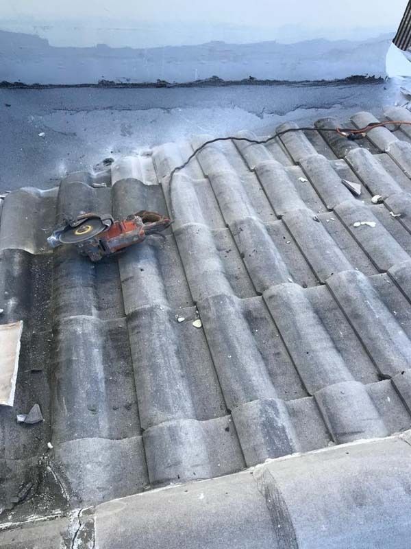 A high-angle view of a gray concrete tile roof with an orange power saw sitting near an edge with dark waterproof sealant.