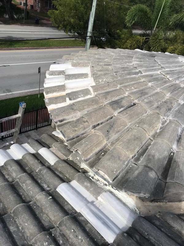 A high-angle view of a tiled roof showing a rounded section under repair with white sealant visible between the tiles.