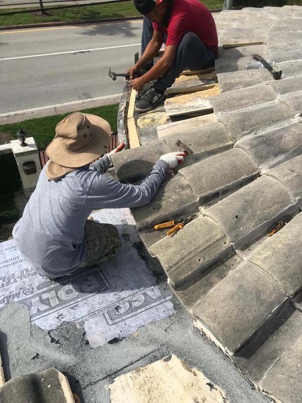 Two workers in hats and work clothes repairing a concrete tile roof on a sunny day.