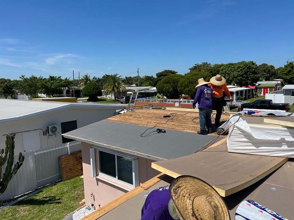Two workers in wide-brimmed hats install roofing materials on a sunny day at a residential property.