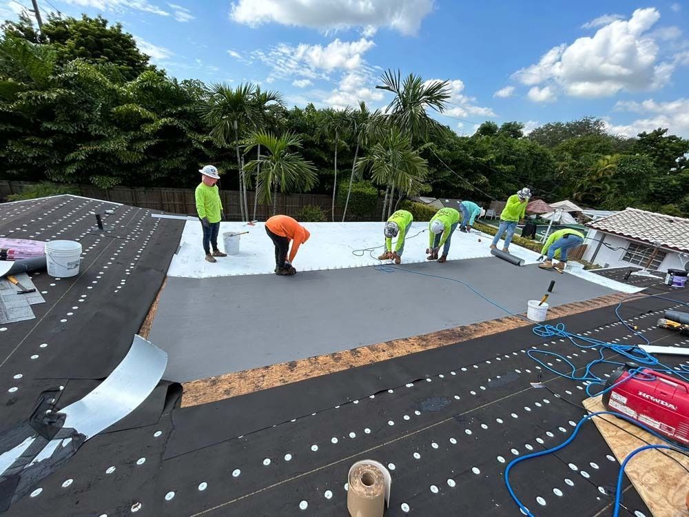 Construction crew members in high-visibility gear install roofing materials on a residential house under a blue sky.