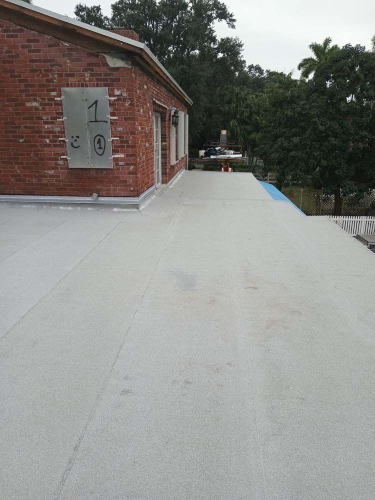 A flat roof covered in light gray material, adjacent to a red brick building wall featuring a metal plaque.