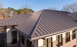 An elevated view of a building with a dark, standing seam metal roof and cream-colored walls with brick accents.