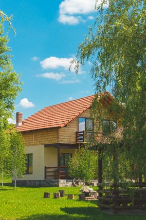 Wooden cabin with red tile roof, surrounded by green trees and grass, under blue sky.