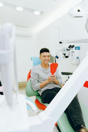 Man smiles, holding a mirror in a dental chair. Bright, modern dental office.